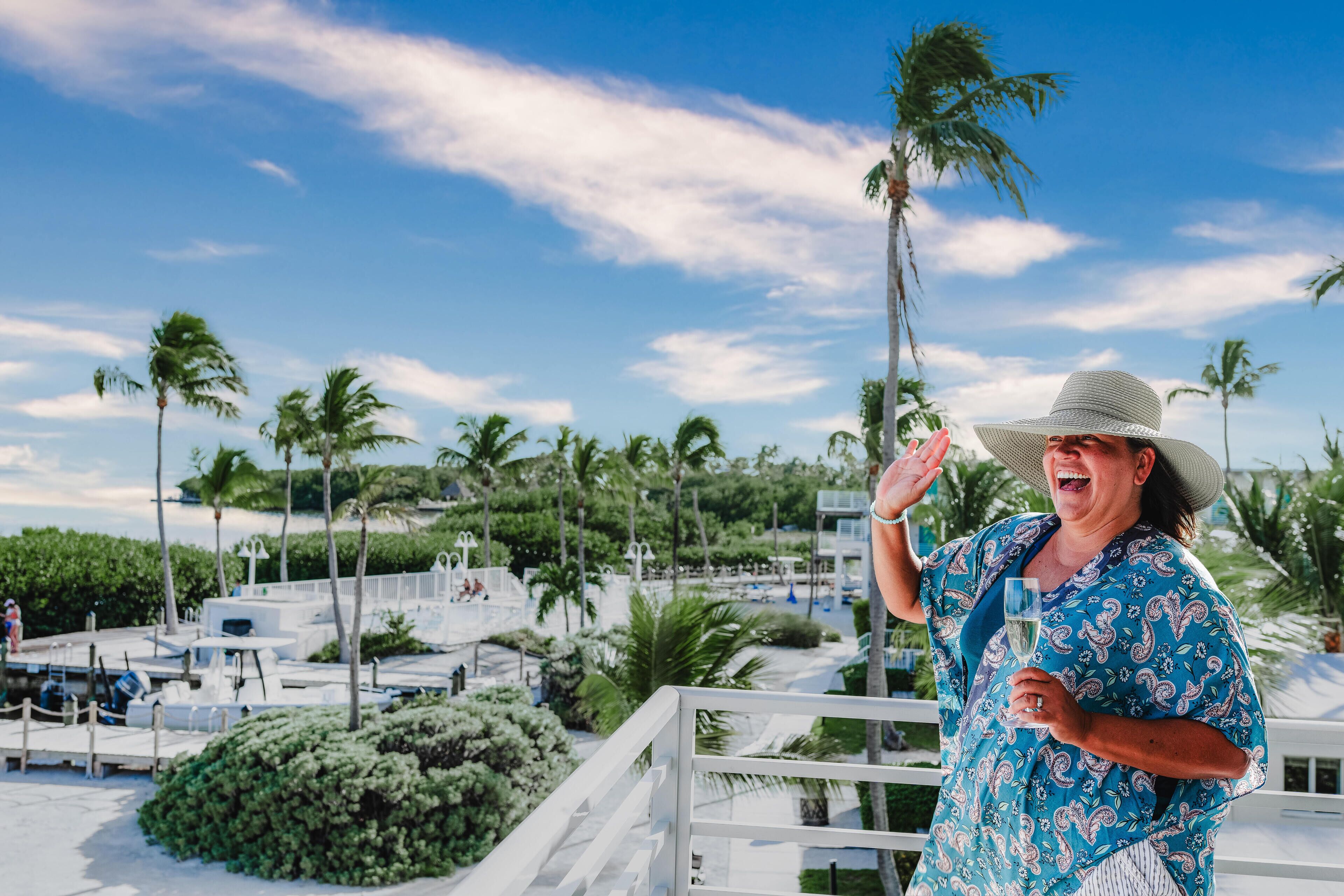 A person on a balcony with a view of palm trees and a pool area.