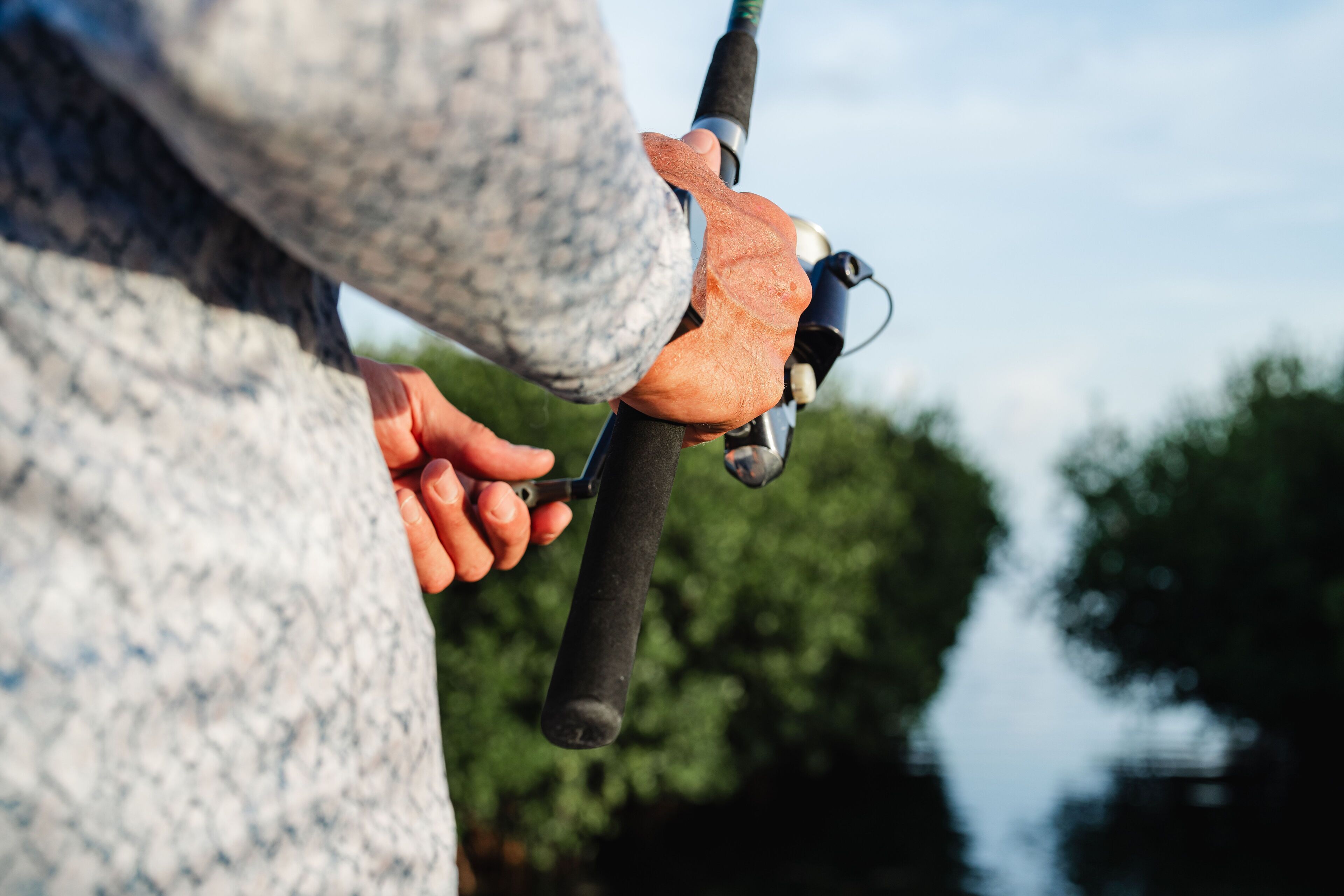 A close-up of a person's hands holding a fishing rod with a bird perched on it.