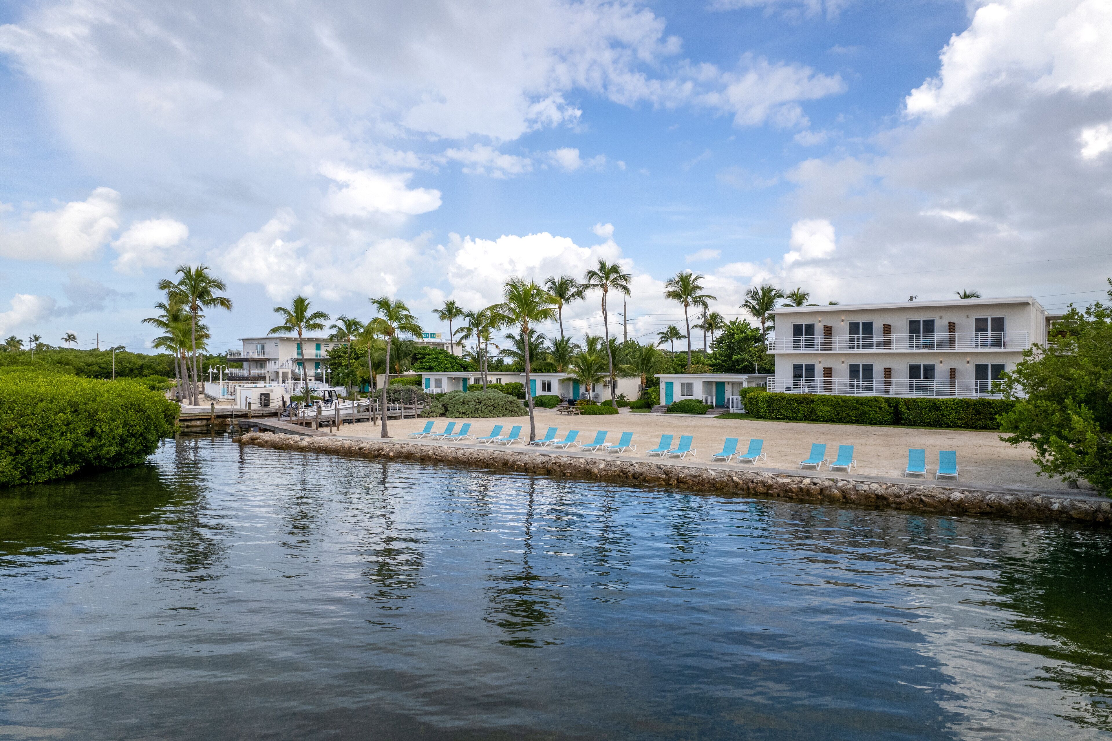 A waterfront hotel with a poolside area, palm trees, and a building with multiple balconies.