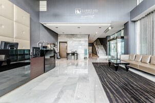 Un moderno vestíbulo de hotel con una recepción, una zona de estar y una escalera que lleva a los pisos superiores.