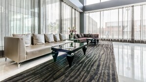 Un salon spacieux avec une grande fenêtre, un canapé, une table basse et un tapis à motifs.