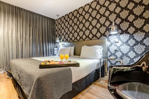 Una habitación de hotel con cama, una bandeja de desayuno, una silla y papel tapiz estampado.
