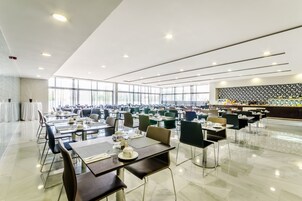Un comedor amplio con varias mesas y sillas, ventanas grandes y una cocina moderna al fondo.