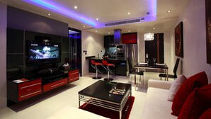 Ein modernes Wohnzimmer mit Flachbildfernseher, roten und schwarzen Möbeln, einem Essbereich mit Bar und einer Küche mit roten Schränken.
