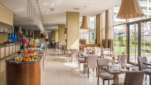 A modern hotel lobby with a buffet, dining tables, and large windows offering a view of the outdoors.