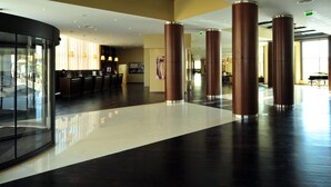 A spacious lobby with a modern design, featuring a glass wall, a reception area, and multiple seating arrangements.