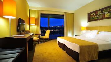 Una camera d'albergo con un letto, una scrivania, una sedia e un'ampia finestra vista città di notte.