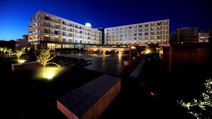 A multi-story hotel with a pool area, outdoor seating, and a well-lit entrance.