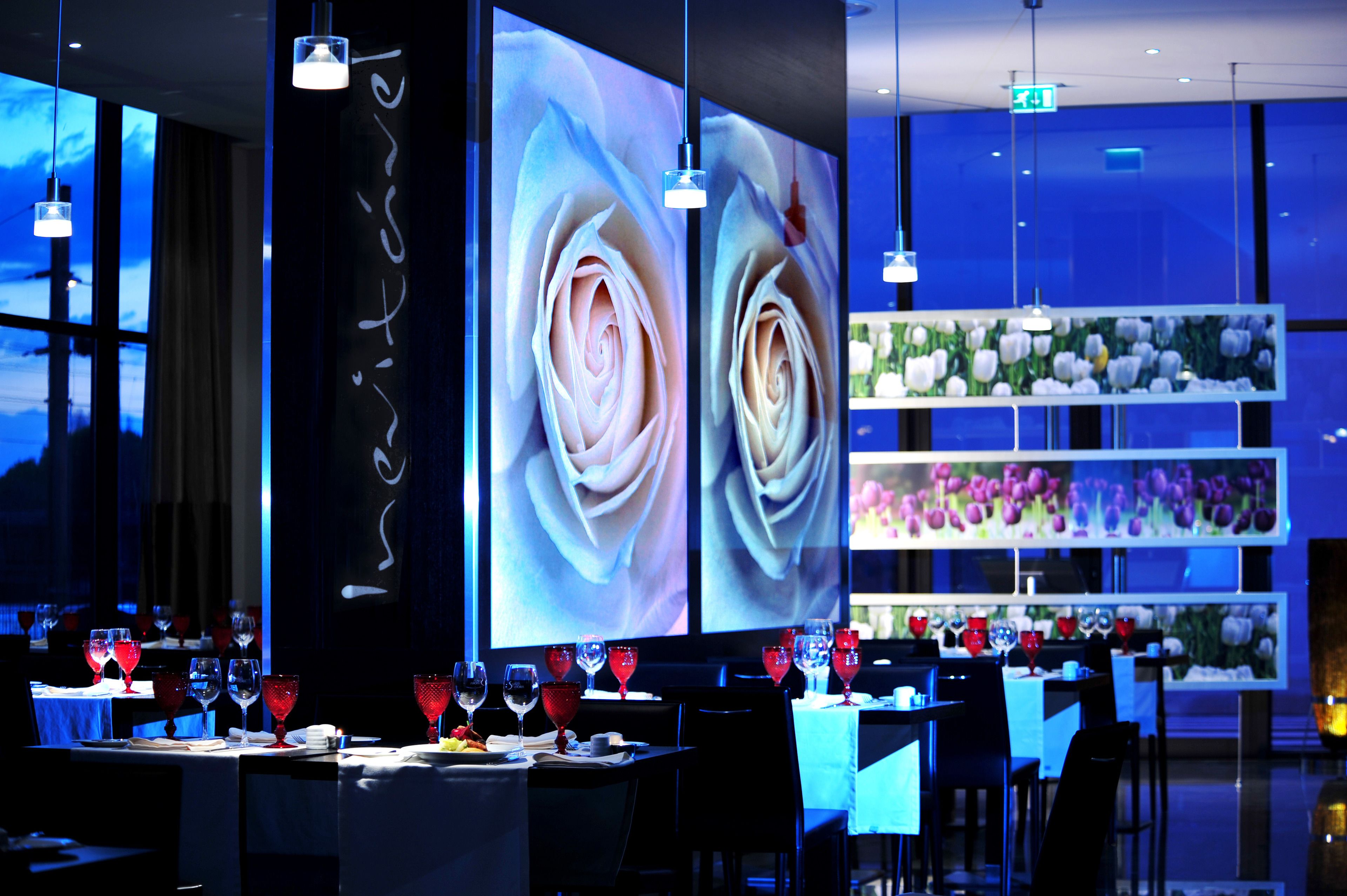 A restaurant with tables set for dining, large floral wall art, and hanging pendant lights.