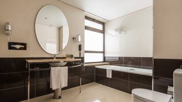 A modern bathroom with a large oval mirror, a sink, a toilet, and a bathtub.