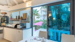 Una cocina moderna con barra desayunadora, refrigerador lleno de bebidas y comedor con mesa dispuesta para dos.