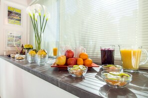 Una presentación de desayuno con varias frutas, jugos y un jarrón de flores sobre una encimera de cocina.