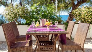 Un juego de mesa de mimbre con mantel morado, dos sillas, una vela y un florero con flores.