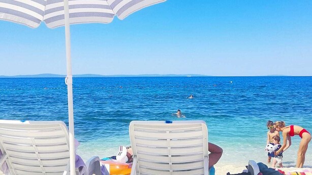 Escena de playa con un paraguas a rayas, dos sillas de playa y una vista despejada del mar.