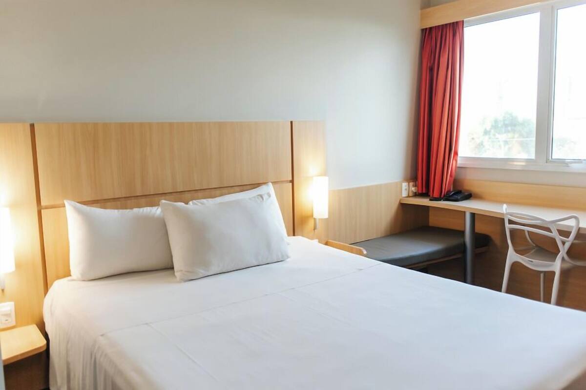 A hotel room with a bed, bedside tables, a desk, and a chair.
