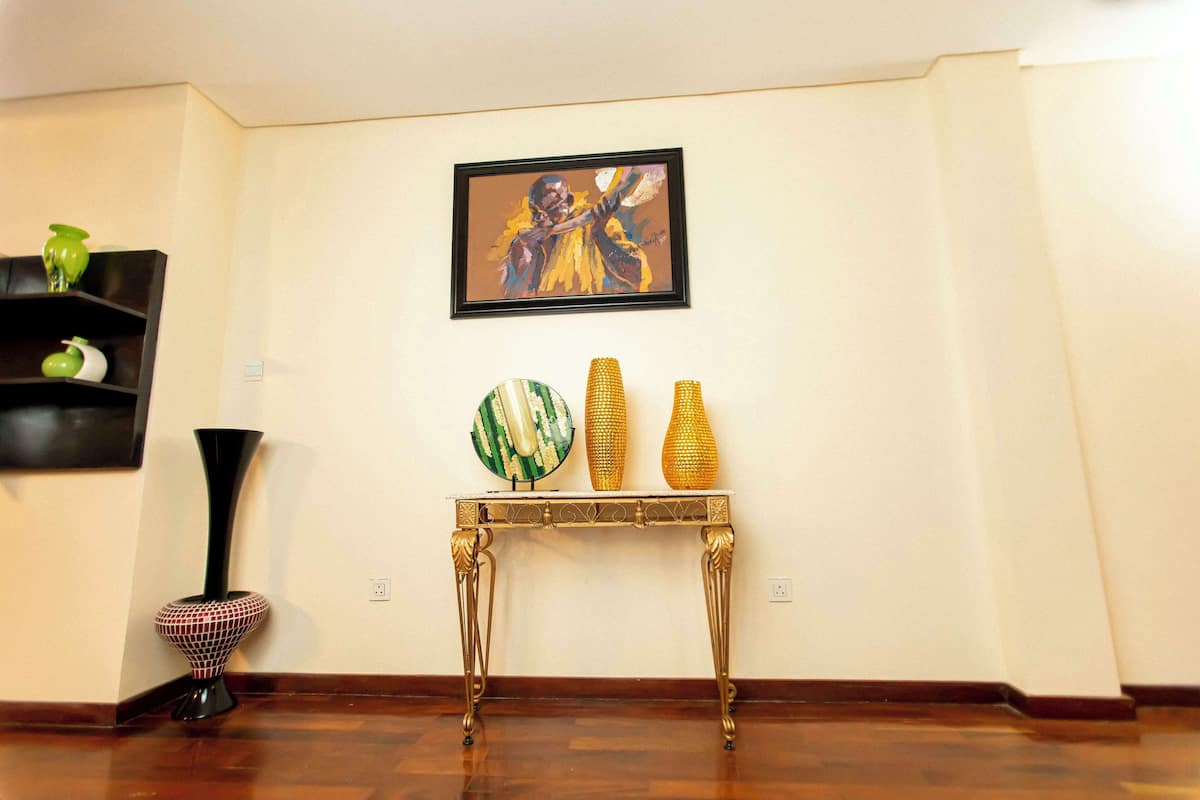 Una habitación con piso de madera, un jarrón negro, un jarrón dorado y un cuadro en la pared.