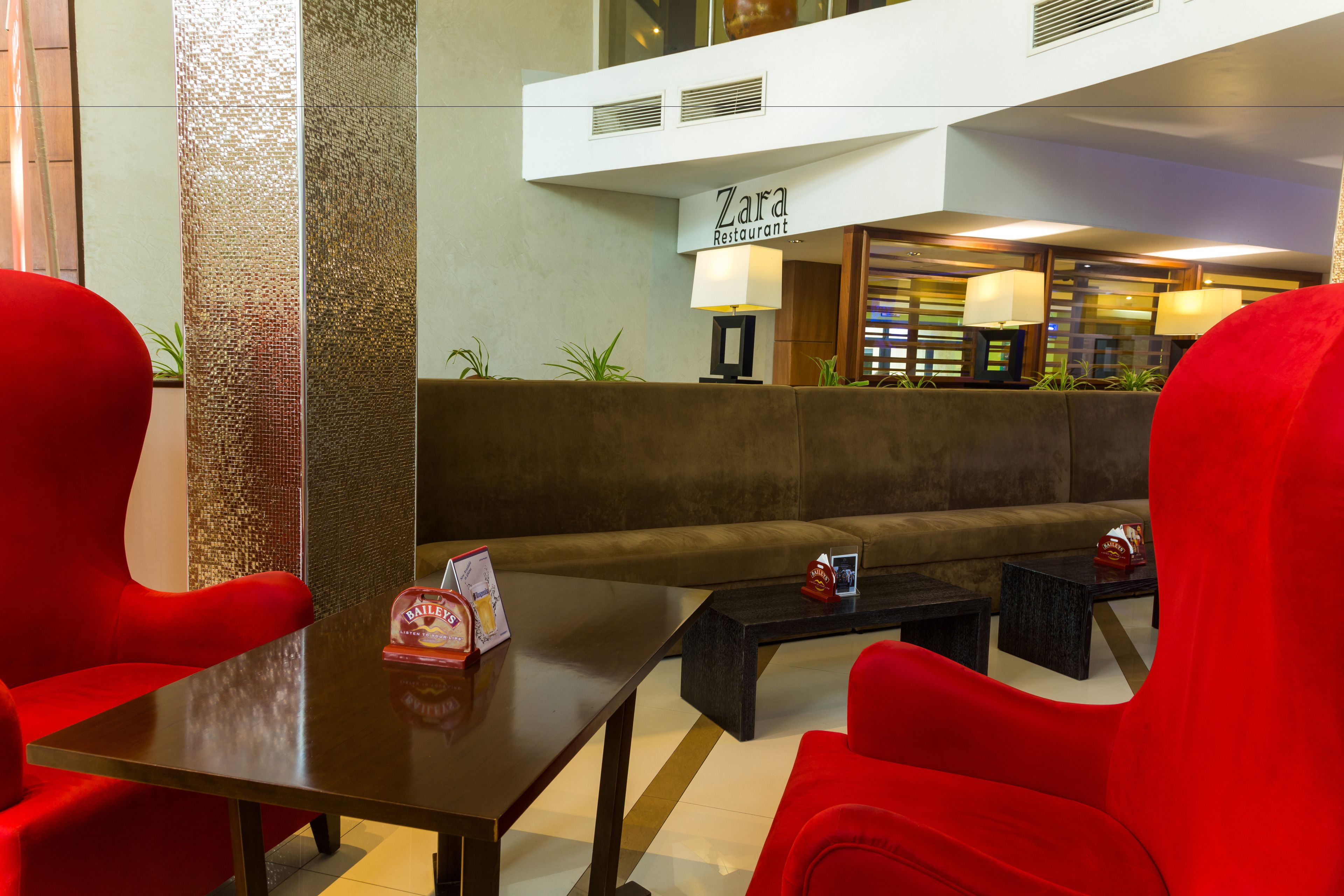 A lobby with a Zara restaurant sign, red seating, and a coffee table with a Bailey's beer box.