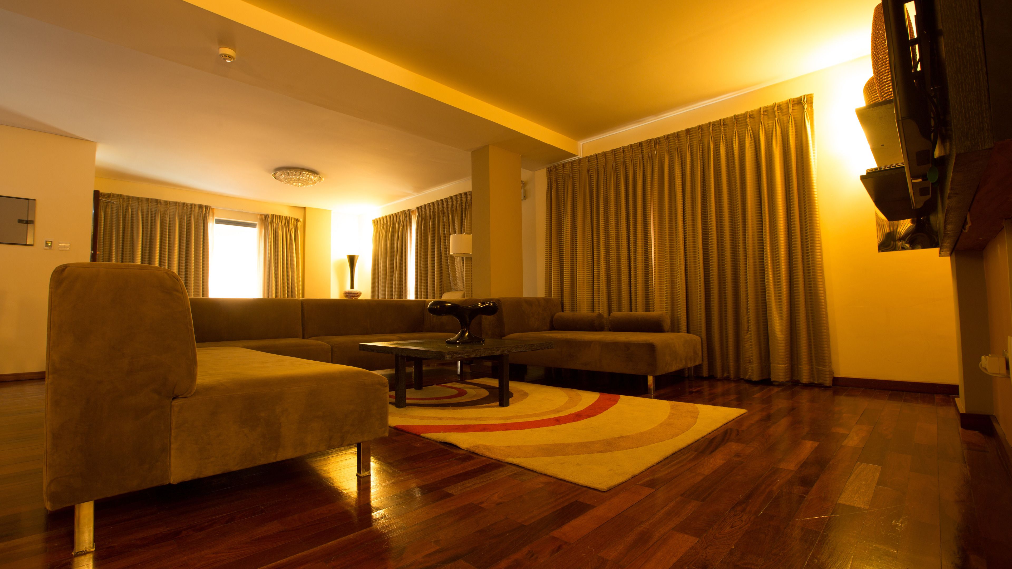 A living room with a sofa, armchair, and coffee table, wooden flooring, and curtains.