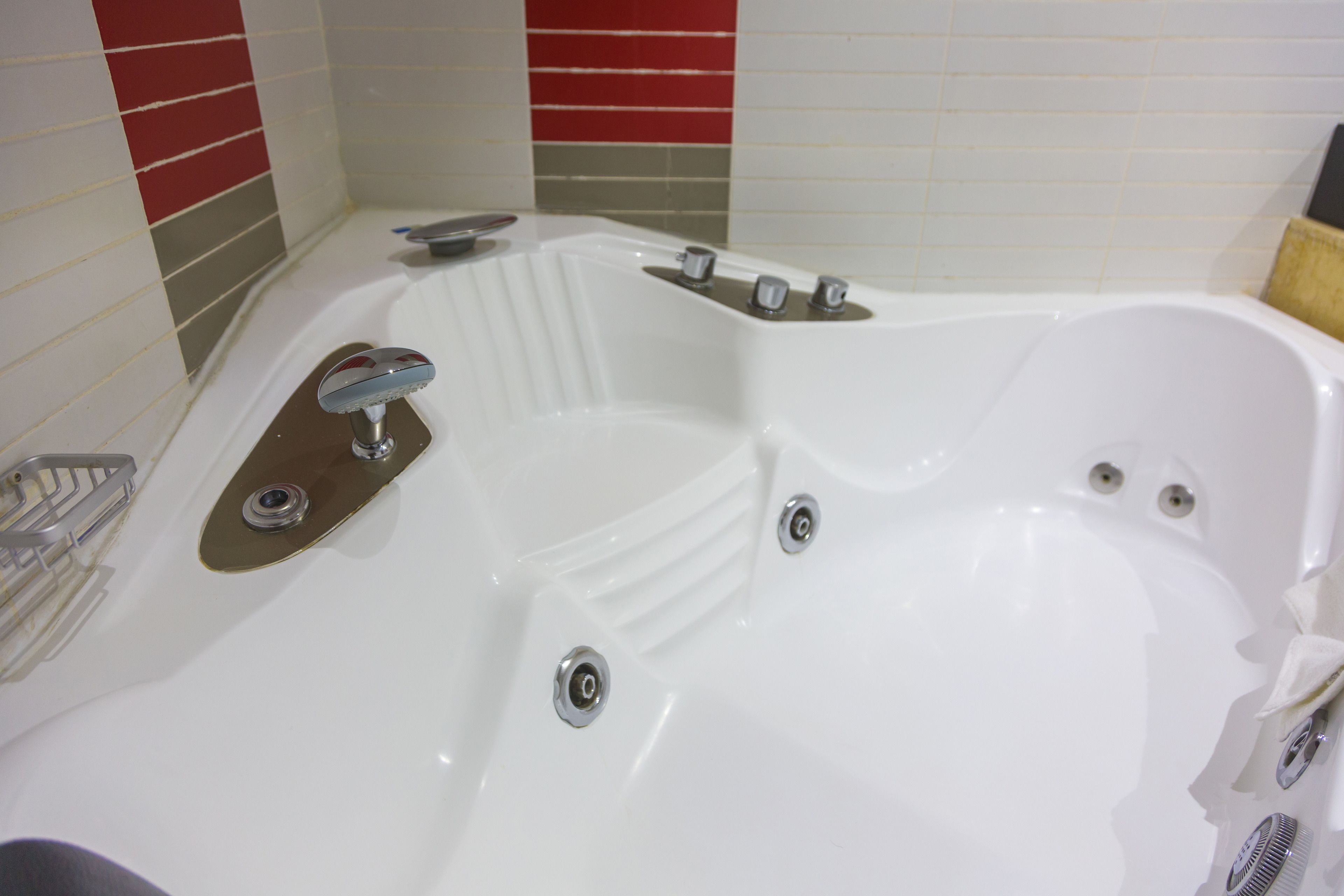 Una bañera blanca con múltiples grifos y un estante integrado.