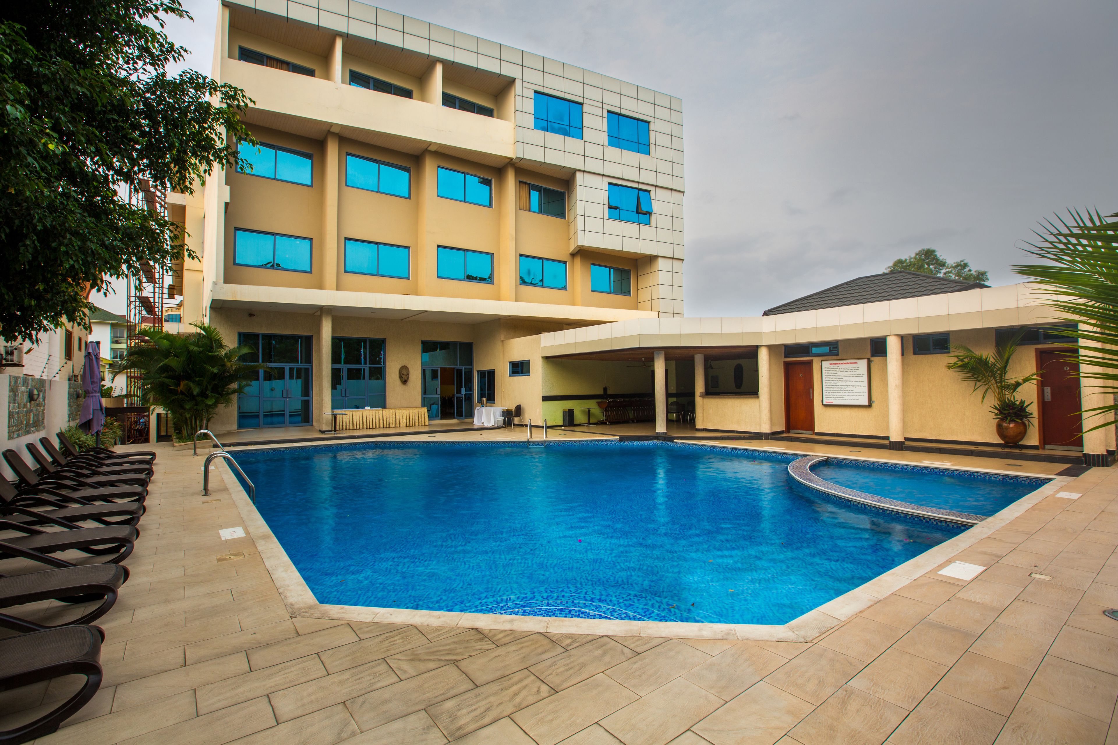 A swimming pool area with lounge chairs and a building with multiple windows.