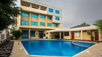 A swimming pool area with lounge chairs and a building with multiple windows.