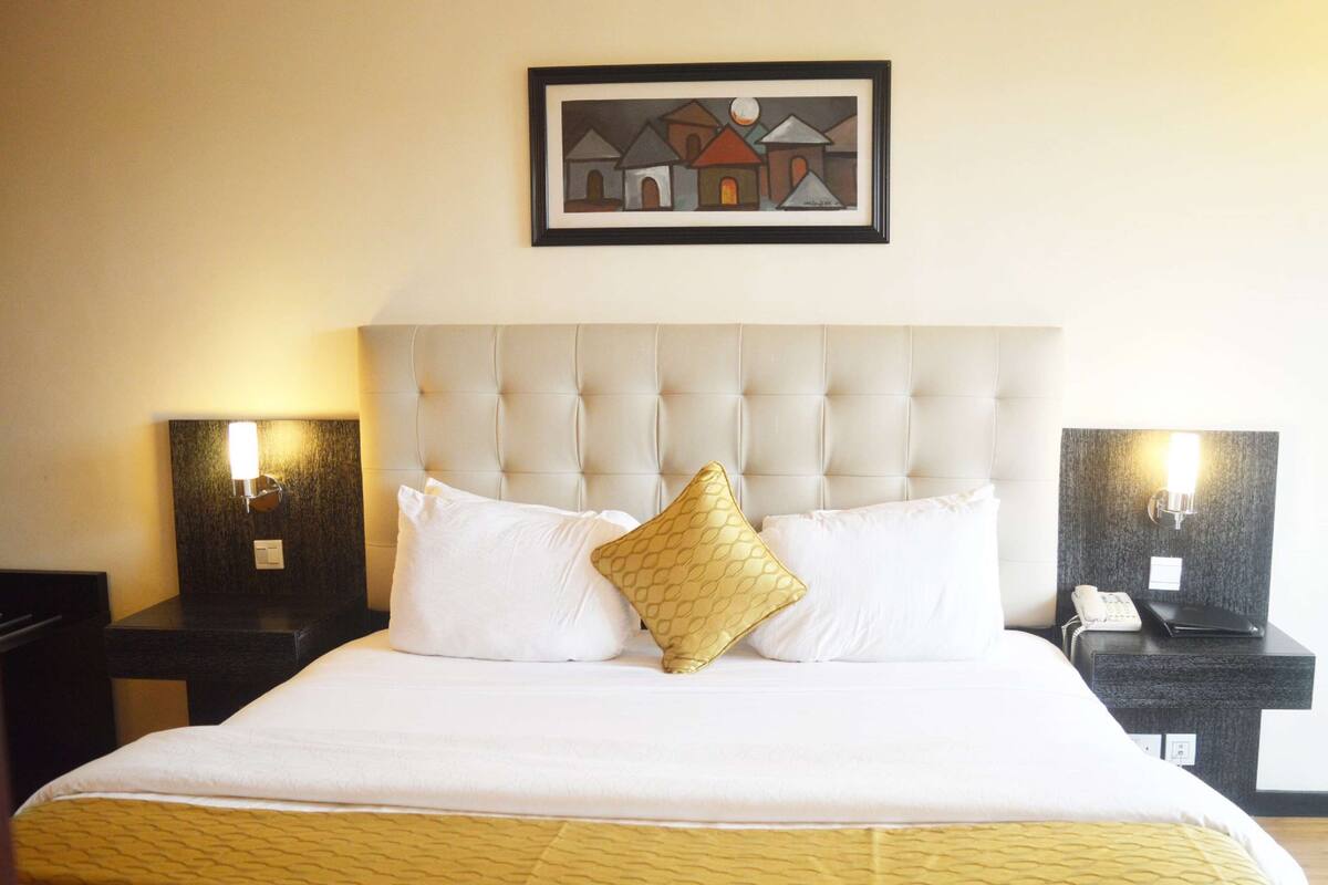 Una habitación de hotel con una cama grande, dos mesitas de noche, un cabecero y una obra de arte enmarcada en la pared.