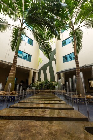 A courtyard with palm trees, a water feature, and a building with large windows. - Best Western Premier Accra Airport Hotel (Accra)