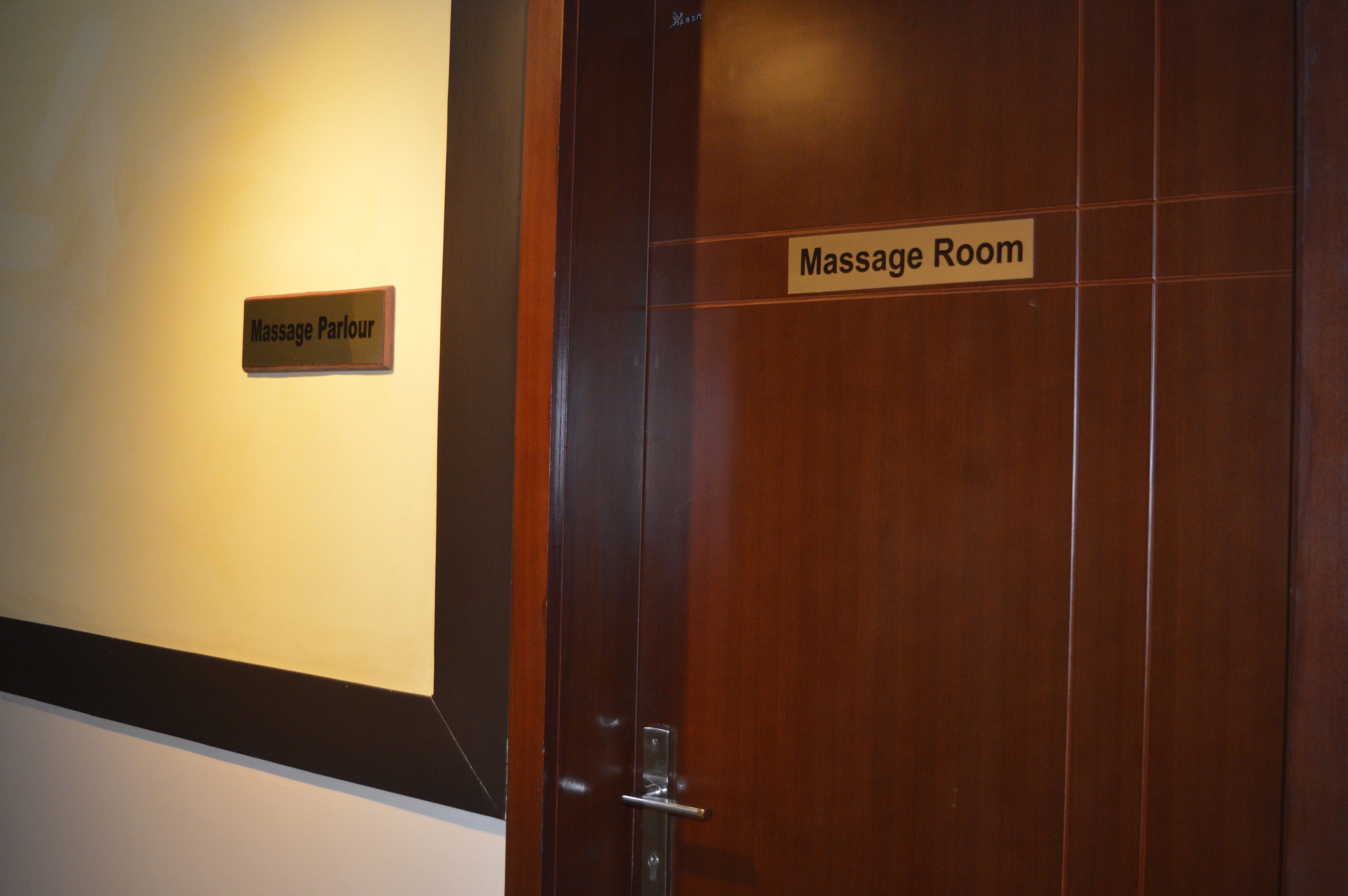 A wooden door with a sign reading "Massage Room" and another sign above it that says "Massage Parlour".