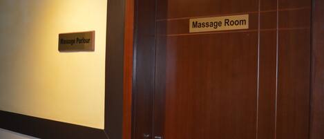 A wooden door with a sign reading "Massage Room" and another sign above it that says "Massage Parlour".