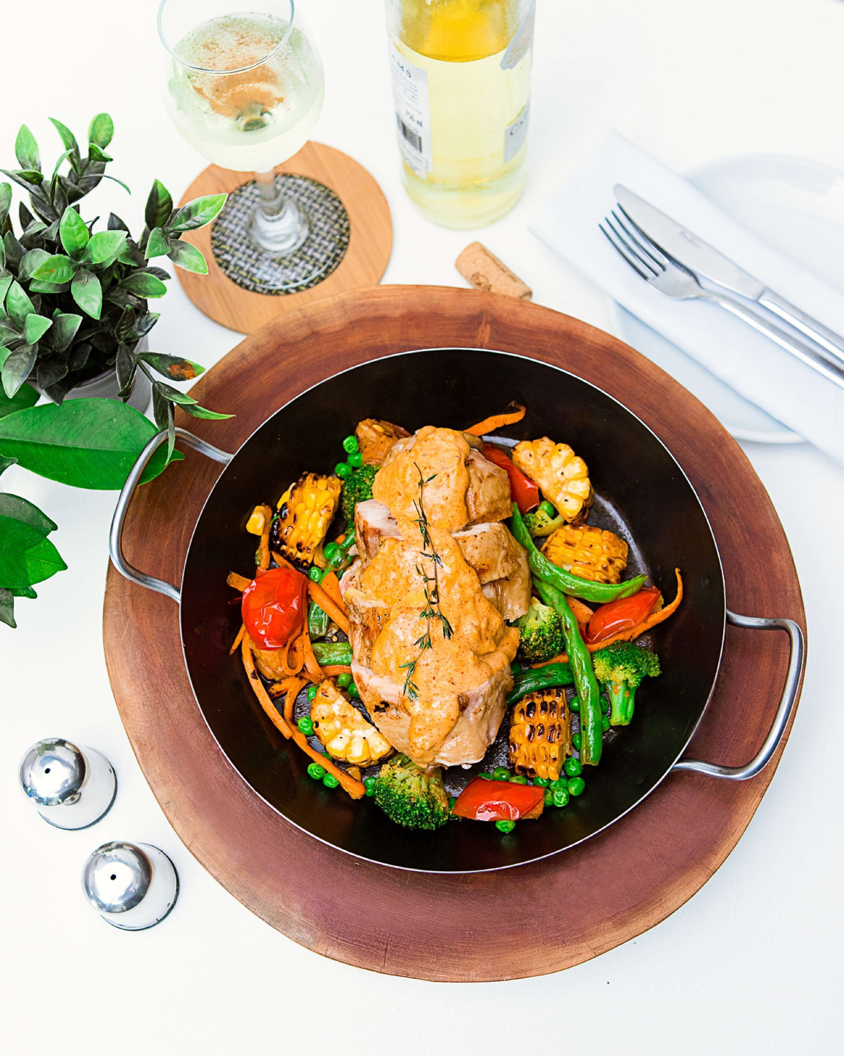 A meal with chicken and vegetables in a black pan on a copper tray.