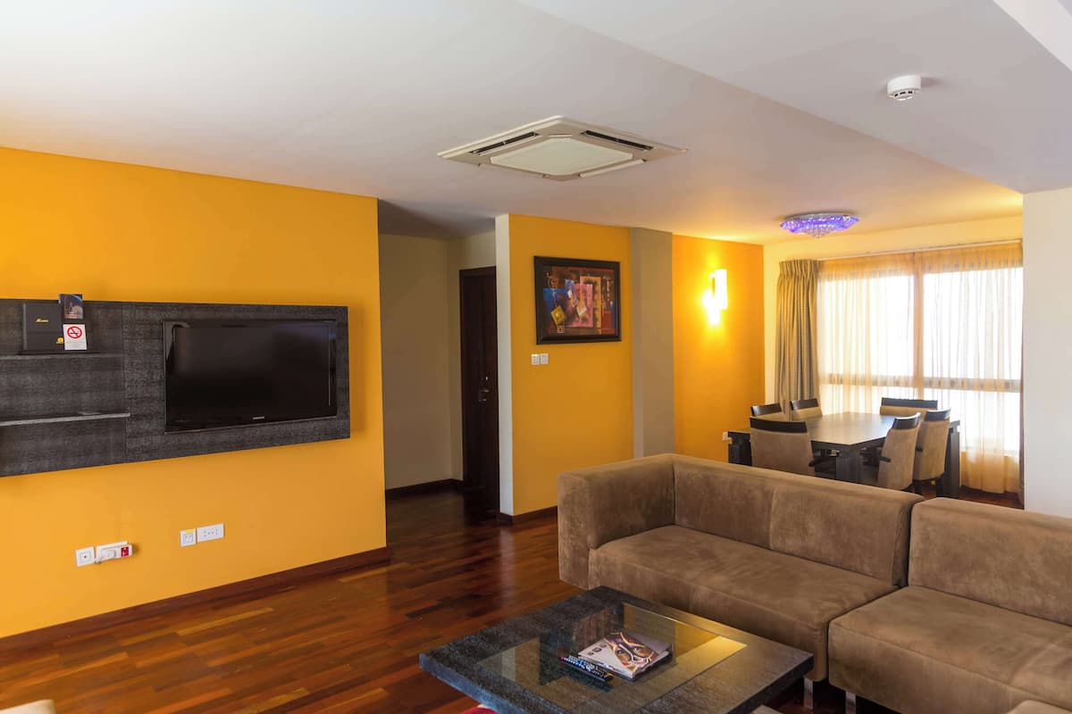 Una sala de estar con televisión de pantalla plana, un sofá, una mesa de centro de vidrio y un comedor con mesa y sillas.