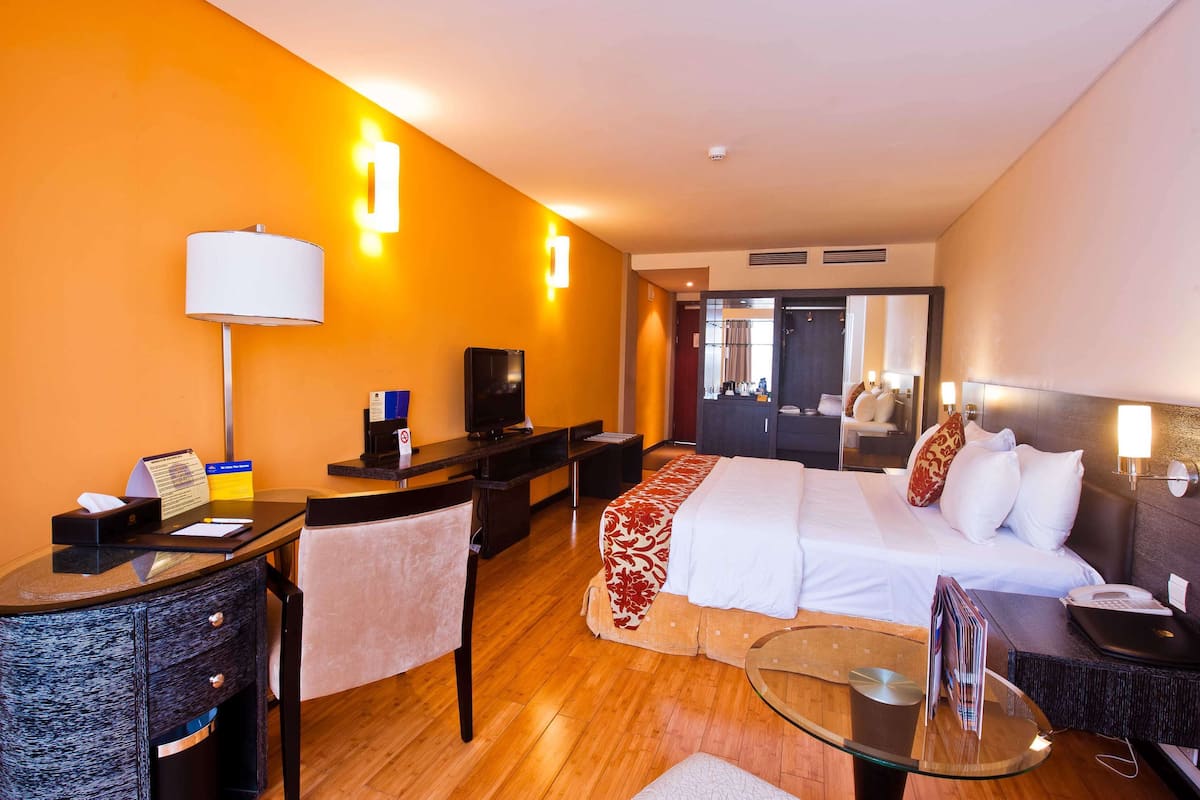 Habitación de hotel con cama, escritorio, silla y una mesa de vidrio.