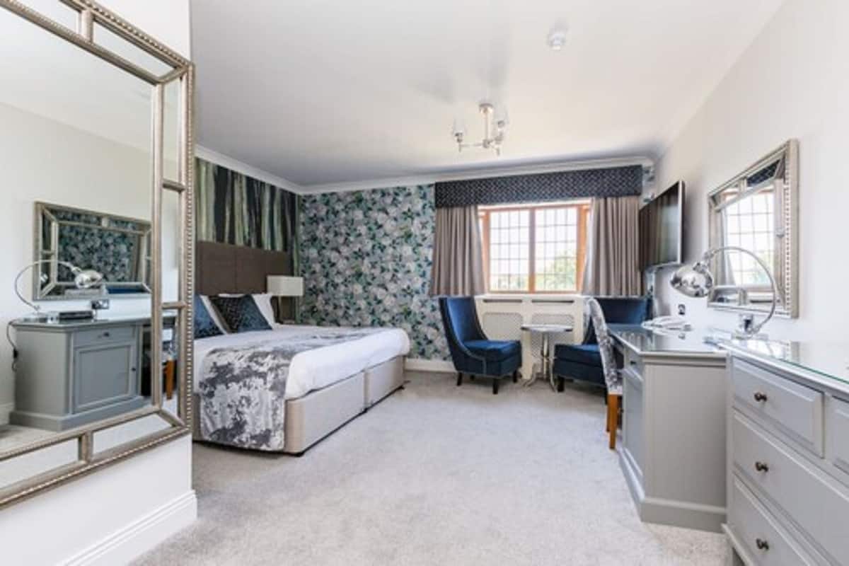A bedroom with a bed, a desk, a chair, a dresser, and a mirror.