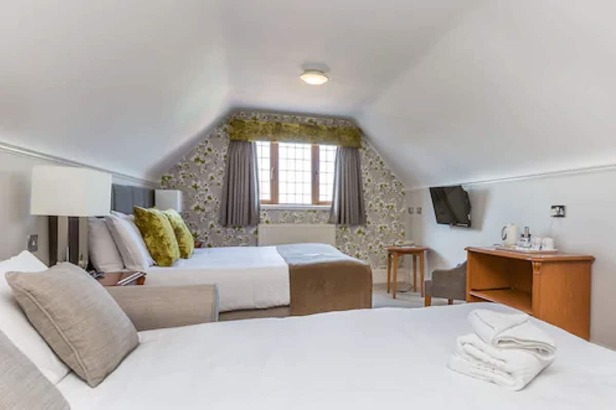 A bedroom with a bed, bedside table, lamp, and a TV on the wall.