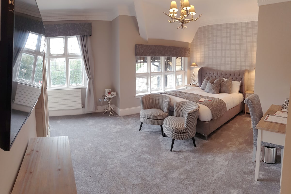 A bedroom with a large bed, two armchairs, a desk, and a chandelier.