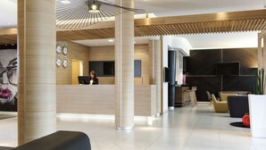 A modern hotel lobby with a reception desk, seating area, and a large wall clock. - Novotel Brussels Centre Midi Station (Brussels)