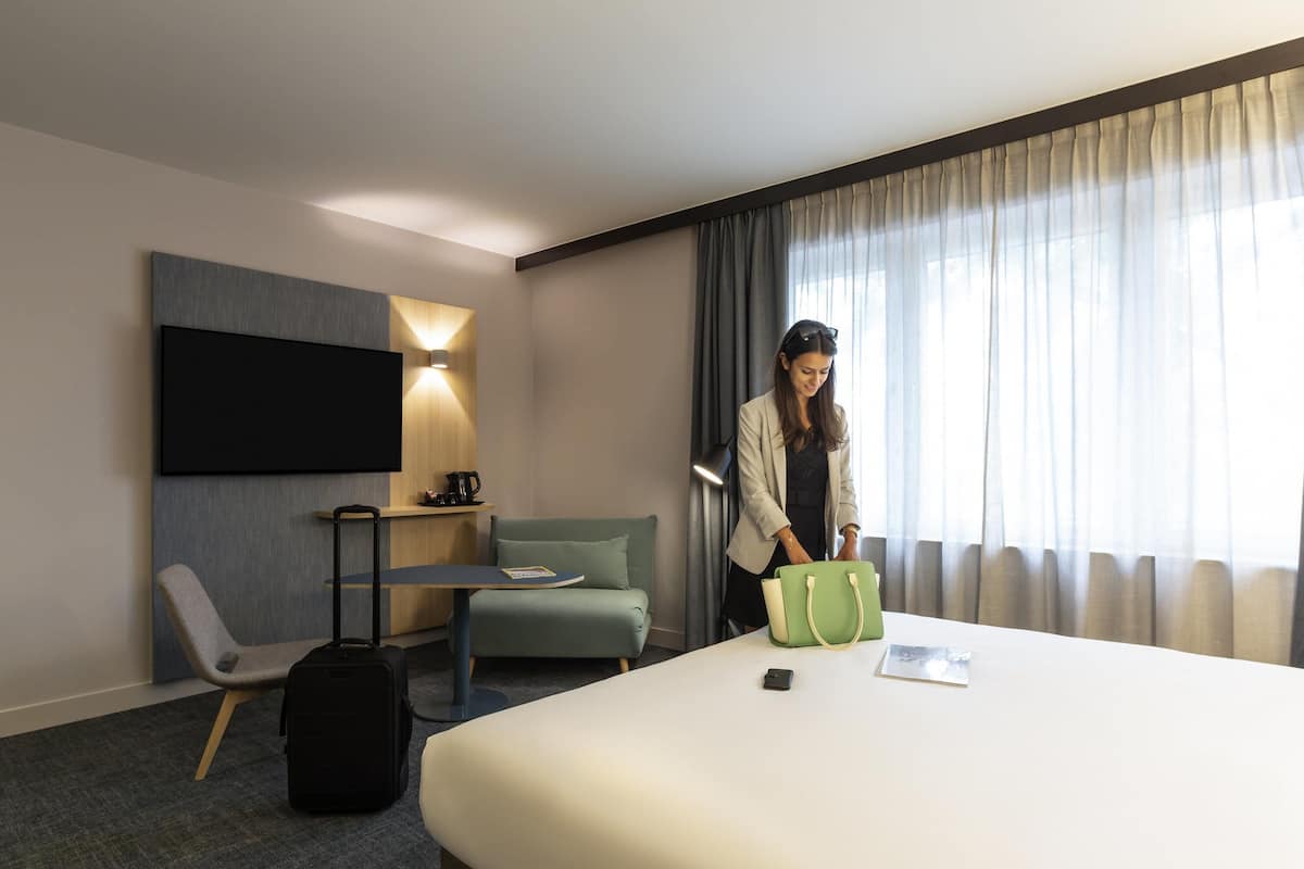 Habitación de hotel con cama, escritorio, silla, televisor y ventana con cortinas.