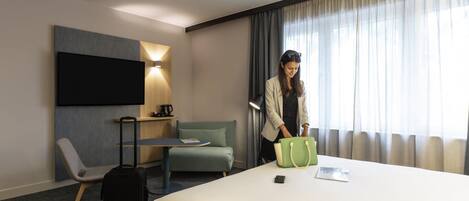 A hotel room with a bed, a desk, a chair, a TV, and a window with curtains.