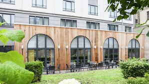 A modern building with large arched windows and a wooden facade, surrounded by a well-maintained garden with hydrangeas. - Novotel Brussels Centre Midi Station (Brussels)