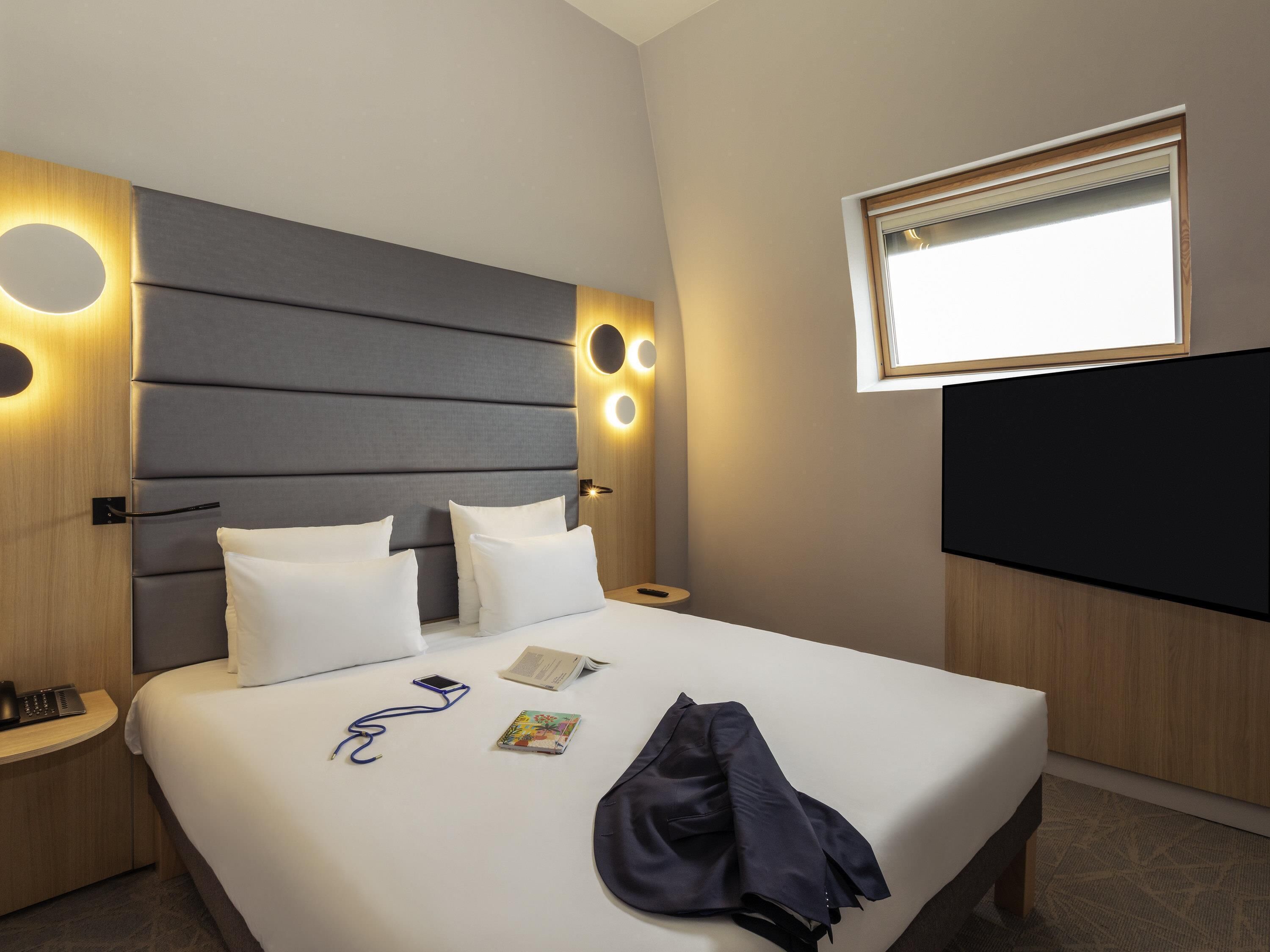 Una habitación de hotel con una cama grande, mesitas de noche, un televisor y una ventana con persianas.