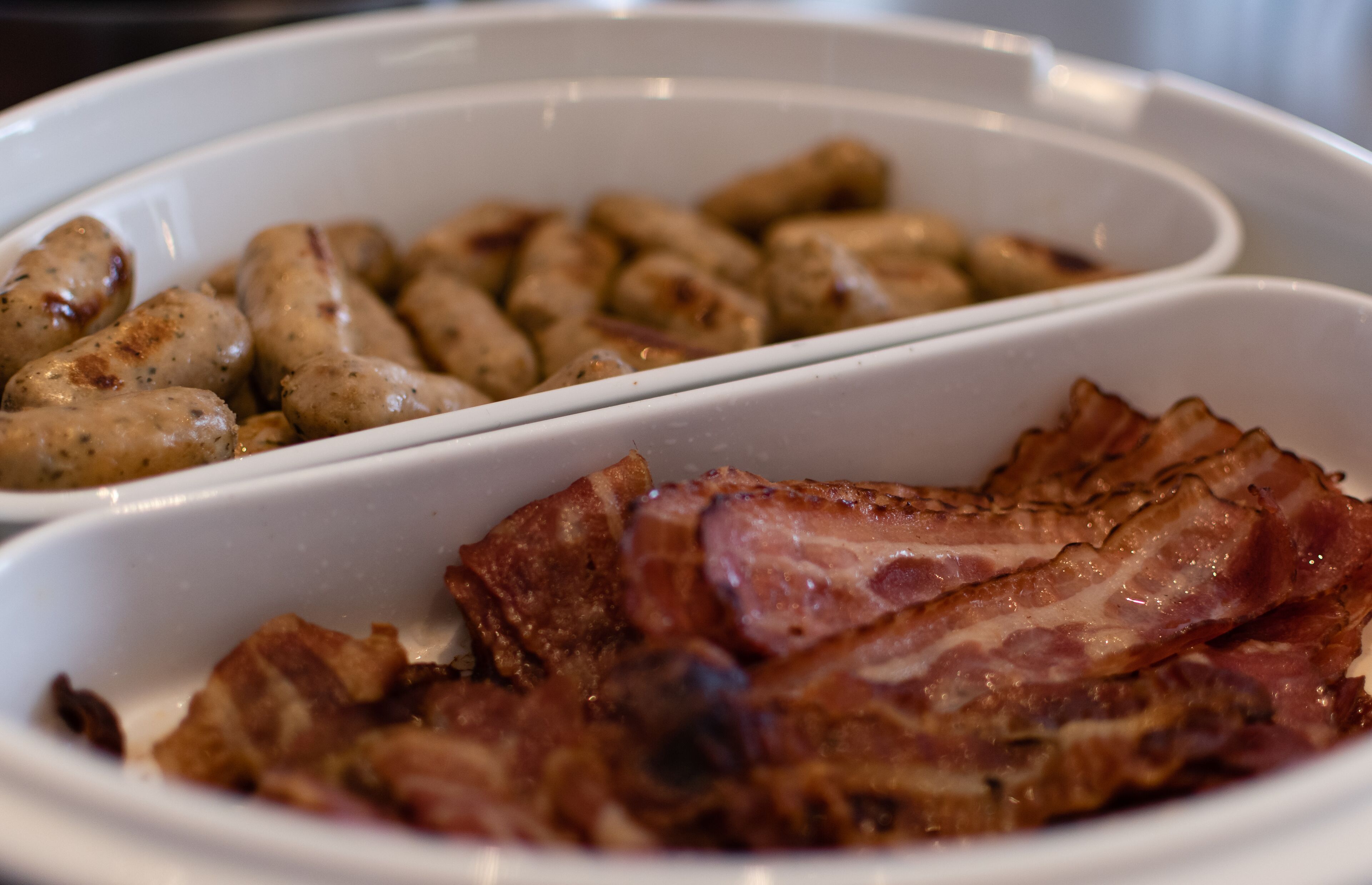A white tray with cooked sausages and bacon.