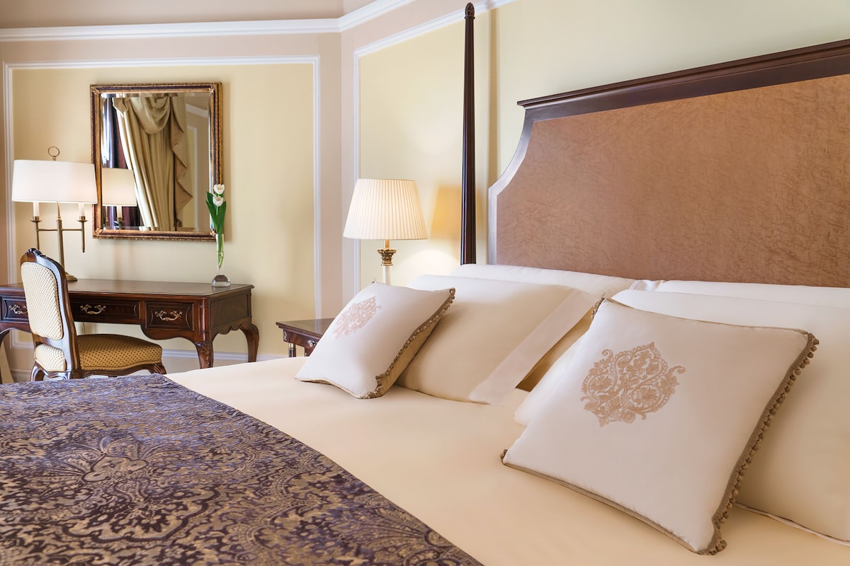 A hotel room with a large bed, two bedside lamps, a desk with a chair, and a mirror on the wall.