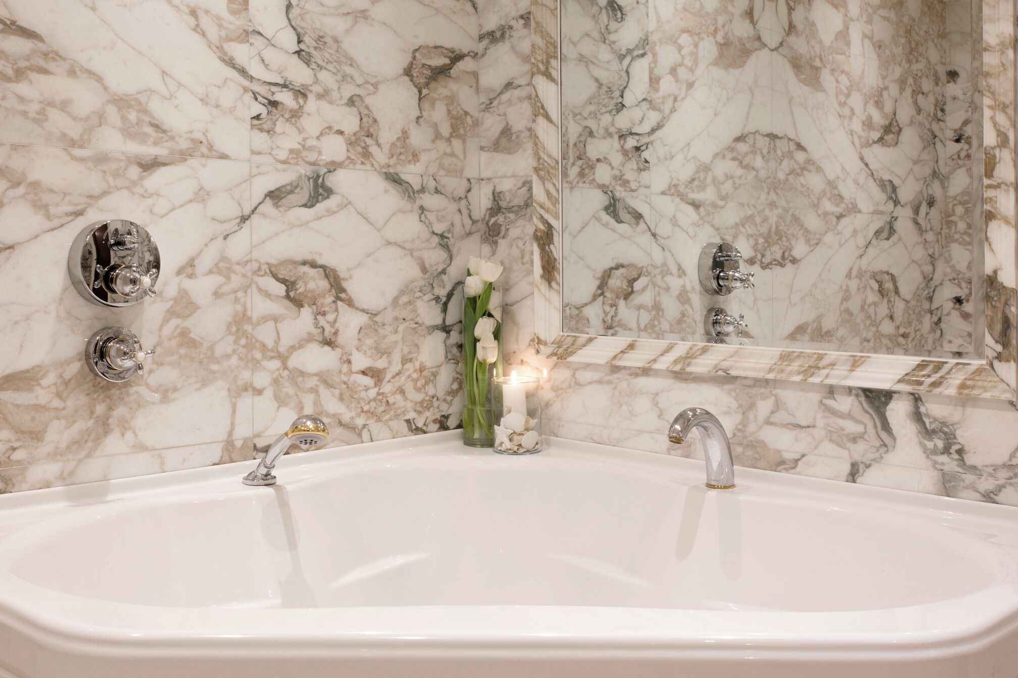 Ein Badezimmer mit einer Marmorwand, einer weißen Badewanne und zwei Chromarmaturen.