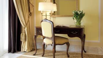 Una habitación con un escritorio de madera, una silla, una lámpara, un espejo y un jarrón con flores.
