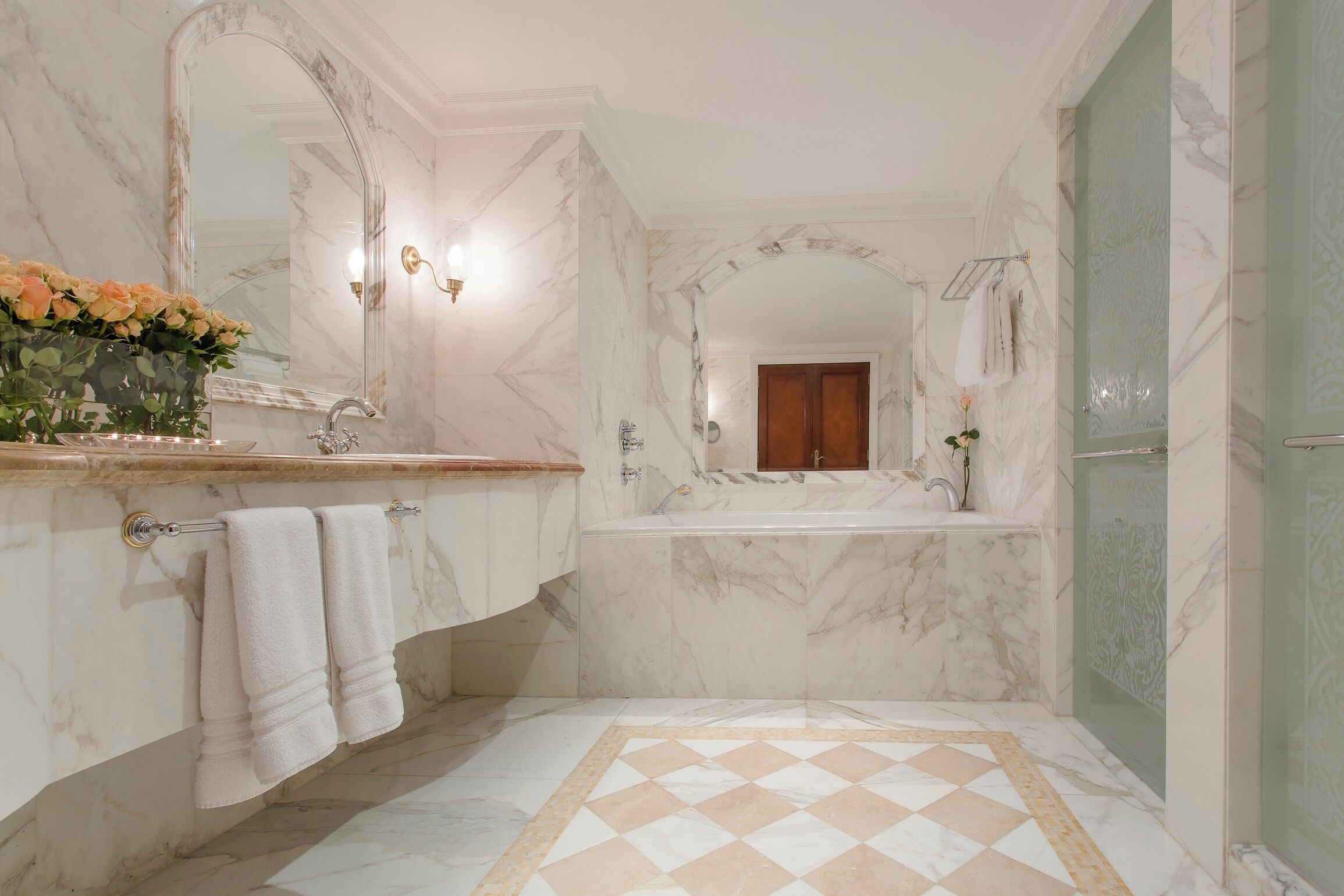 Ein Badezimmer mit Marmorboden, einem großen Spiegel, einem Waschbecken und einer Badewanne.