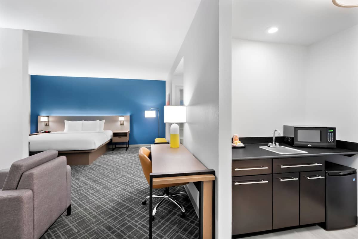 A hotel room with a bed, desk, chair, and kitchenette.