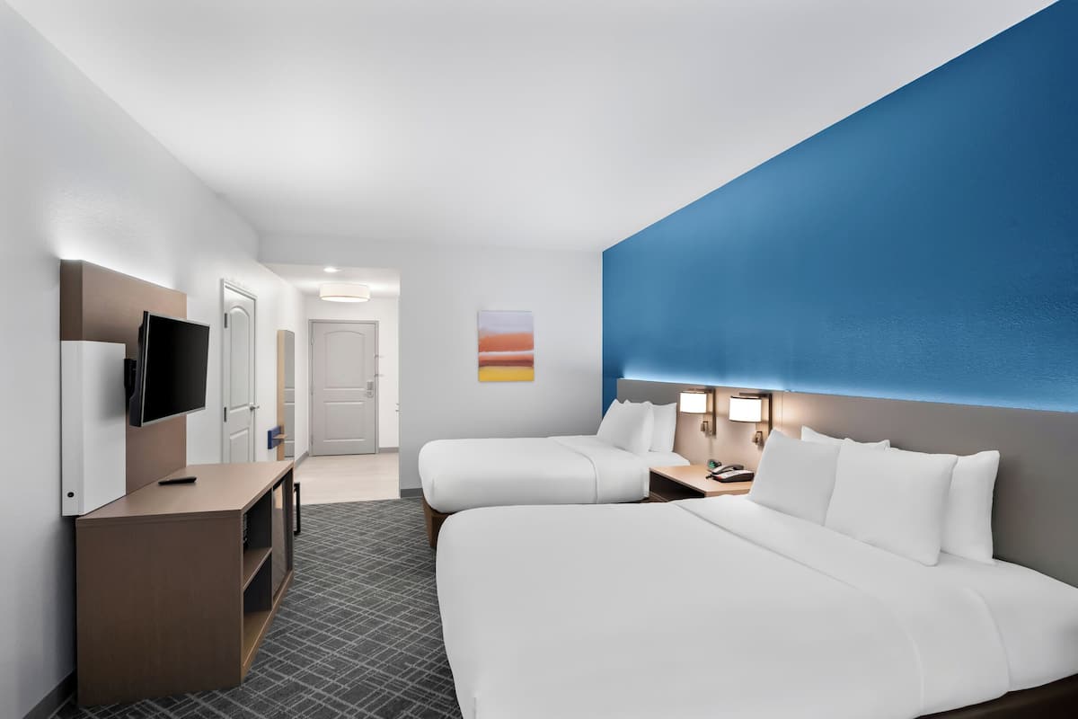 A hotel room with two beds, a desk, a TV, and a painting on the wall.