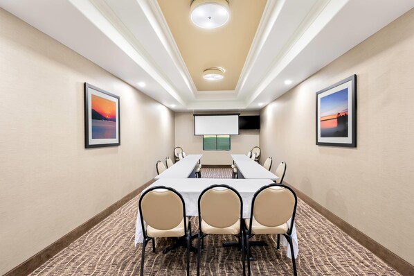A conference room with a long table, chairs, a projector screen, and framed pictures on the walls.