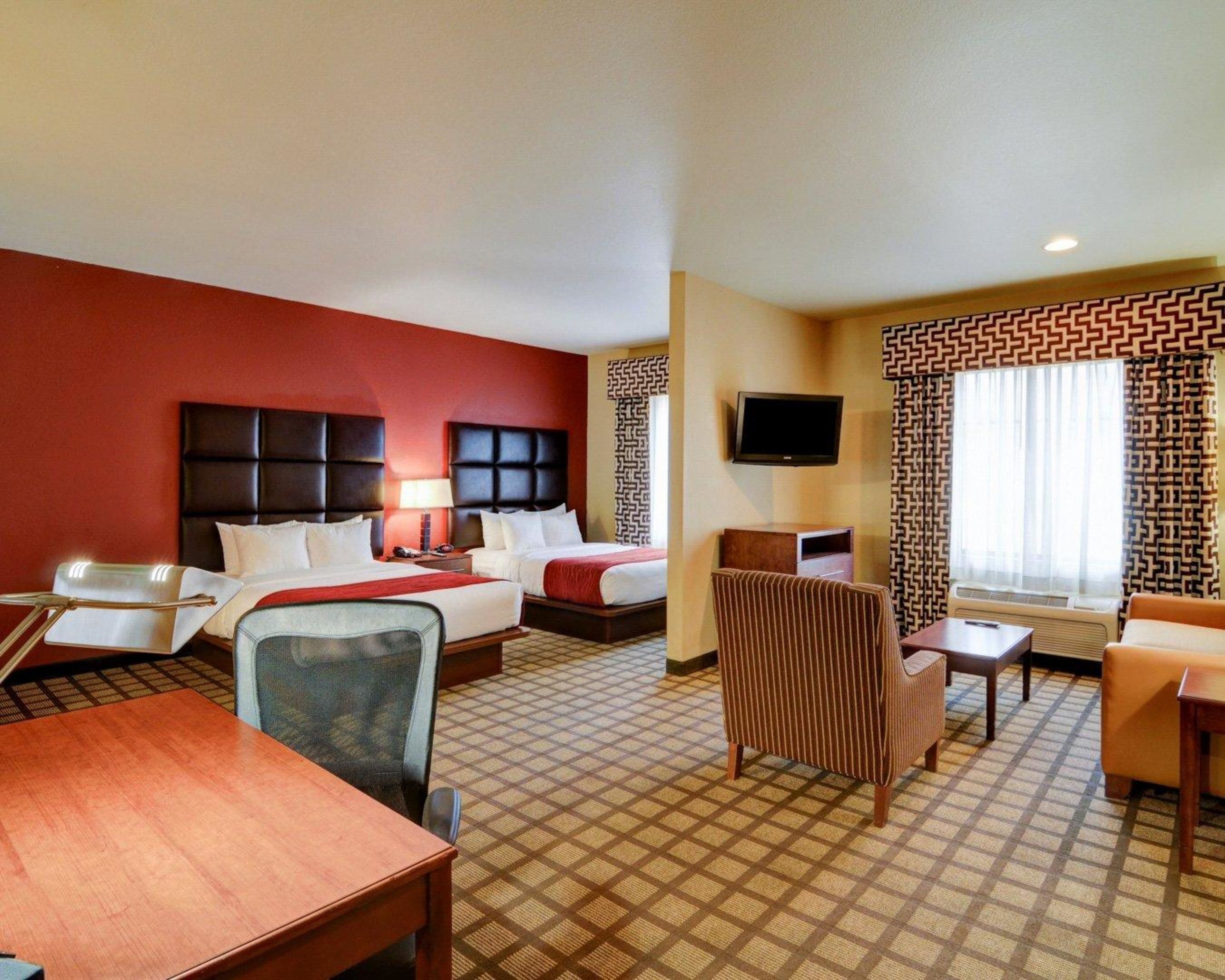 A hotel room with two beds, a desk, a chair, a TV, and patterned curtains.