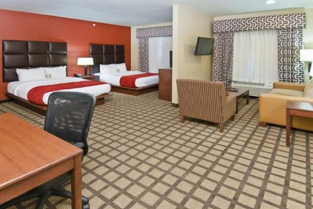 A hotel room with two beds, a desk, a chair, a sofa, and a TV.